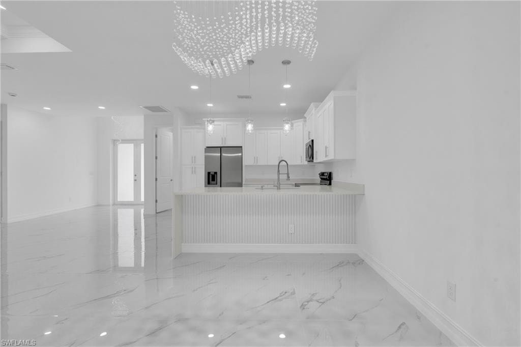 Kitchen featuring recessed lighting, a peninsula, white cabinetry, light marble finish floors, and stainless steel appliances
