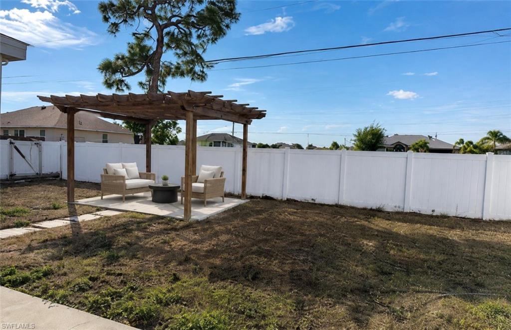 Outdoor pergola with a concrete pad, surrounded by a white privacy fence