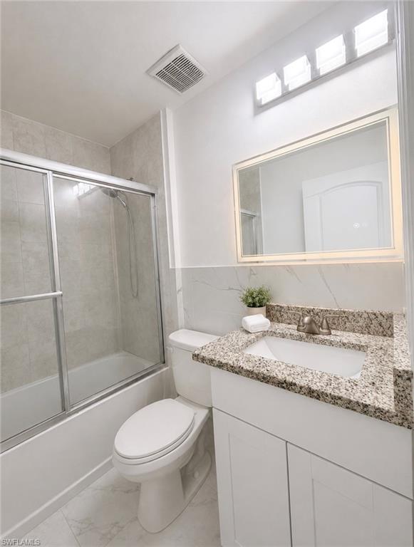 Bathroom featuring a sliding glass shower enclosure, white vanity with a granite countertop, undermount sink, and a framed mirror with overhead lighting
