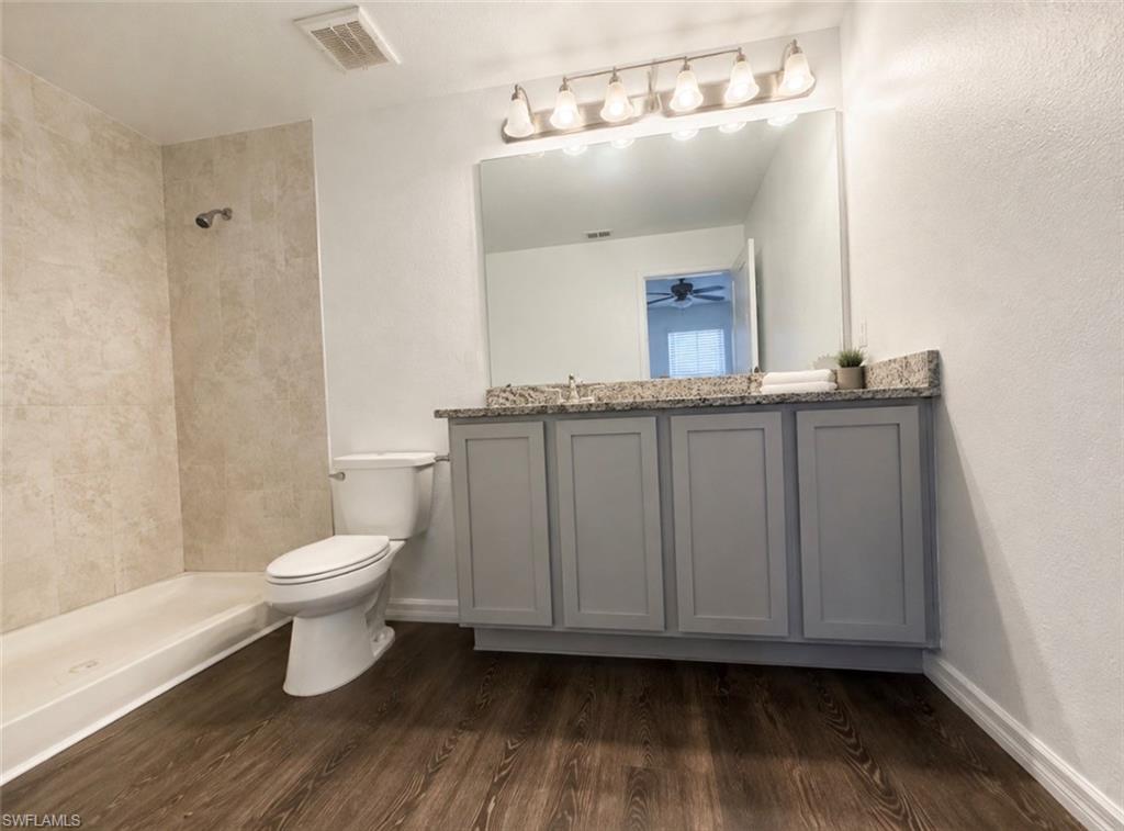 Spacious bathroom featuring a single vanity with gray cabinetry, a light-toned granite-style countertop, and wood-finish flooring