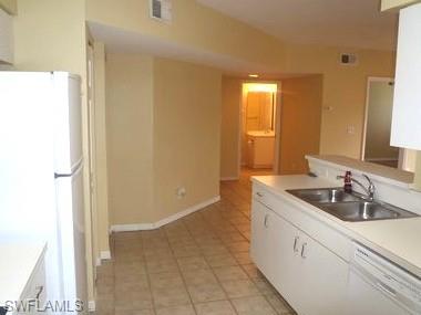 Galley-style kitchen featuring white cabinetry, stainless steel sink, tile flooring, and ample counter workspace