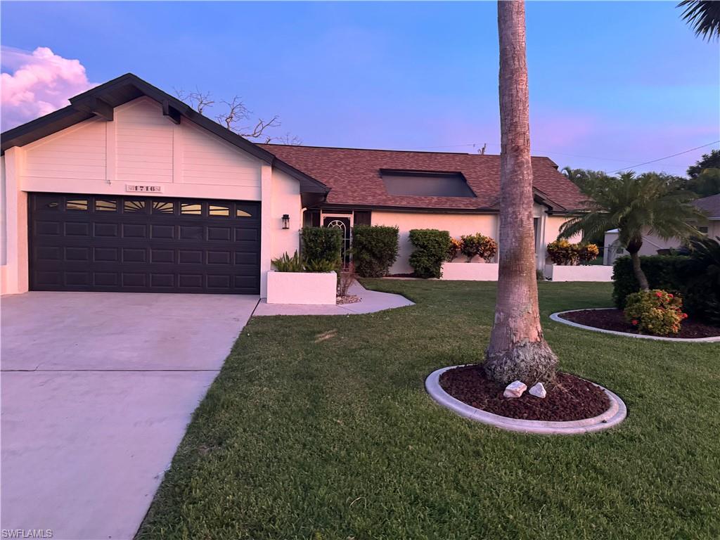 Single-story residence featuring a stucco exterior with a two-car garage, circular driveway, and mature palm tree with defined mulch ring