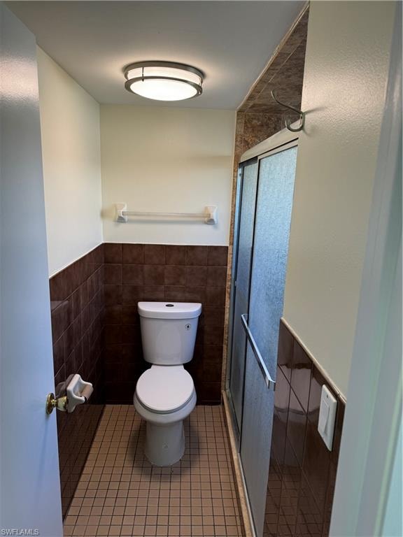Compact powder room featuring a two-piece toilet, tile flooring, dark tile wainscoting, recessed ceiling lighting, and a towel bar