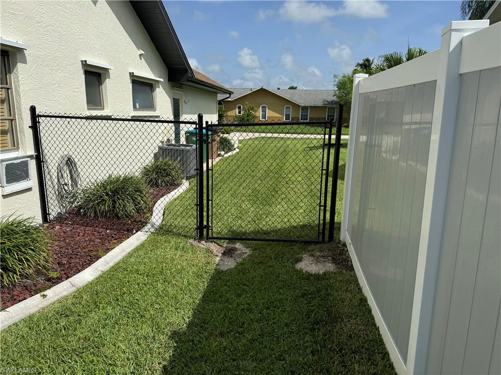 Fenced backyard with mature landscaping, artificial turf lawn, and black aluminum gate entry