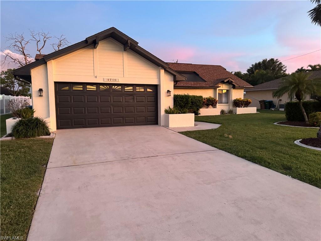 Charming single-story residence featuring a spacious driveway with concrete paving, two-car garage with dark panel doors, and a manicured front lawn