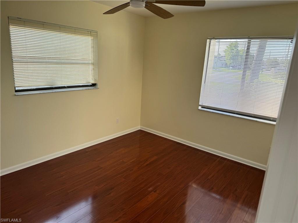 Bright corner bedroom featuring gleaming wood-finish flooring, neutral wall finishes, and abundant natural light from two large windows with cellular blinds