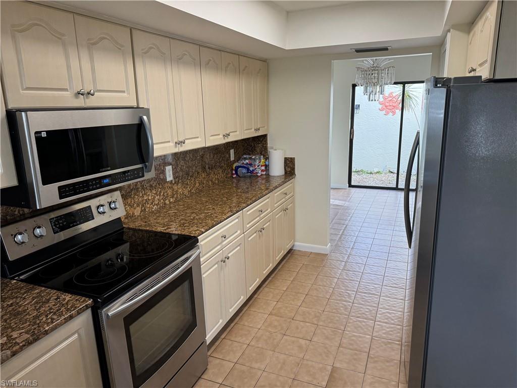 Kitchen featuring extensive cabinetry, granite countertops, stainless steel appliances including an oven and microwave, and tile flooring