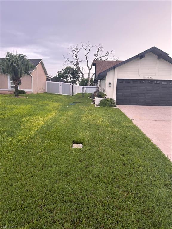 Charming single-story home featuring a manicured lawn, two-car garage with dark finish doors, white vinyl fencing, and mature landscaping including a weeping willow tree