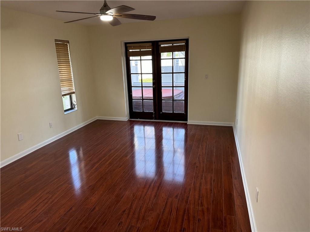 Spacious room featuring rich wood-finish flooring with a polished sheen, neutral walls, and abundant natural light from dual glass doors with black frames