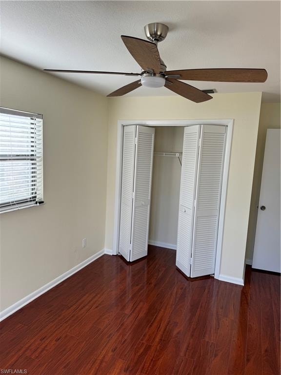 Spacious bedroom featuring rich wood-finish flooring, ceiling fan with integrated lighting, large closet with louvered bifold doors, and abundant natural light from windows with plantation shutters