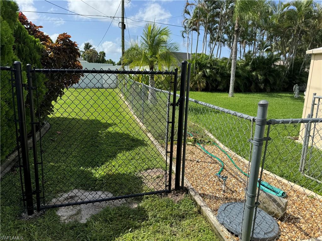 Black chain link fencing enclosing a grassy area with mature trees and landscaping