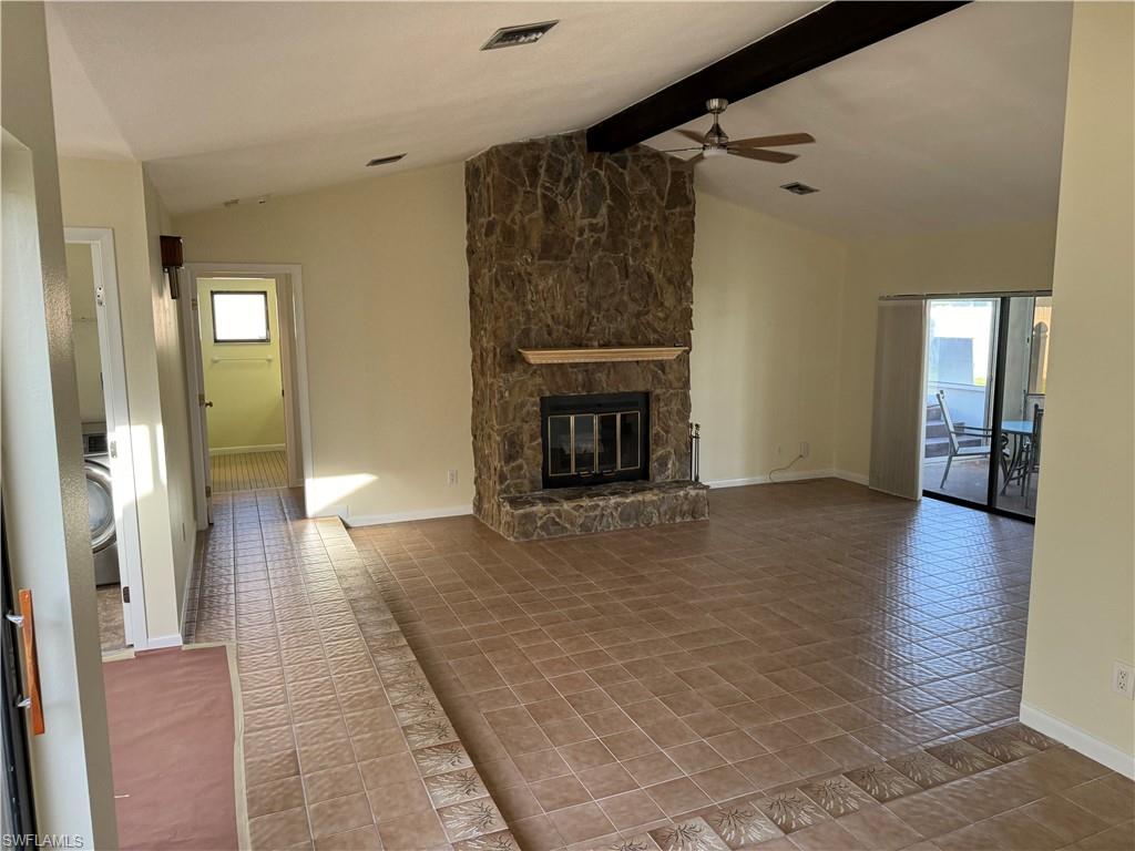 Spacious open-concept living area featuring a striking stone-clad fireplace with metal surround, terracotta tile flooring throughout, and abundant natural light from multiple glass doors and windows