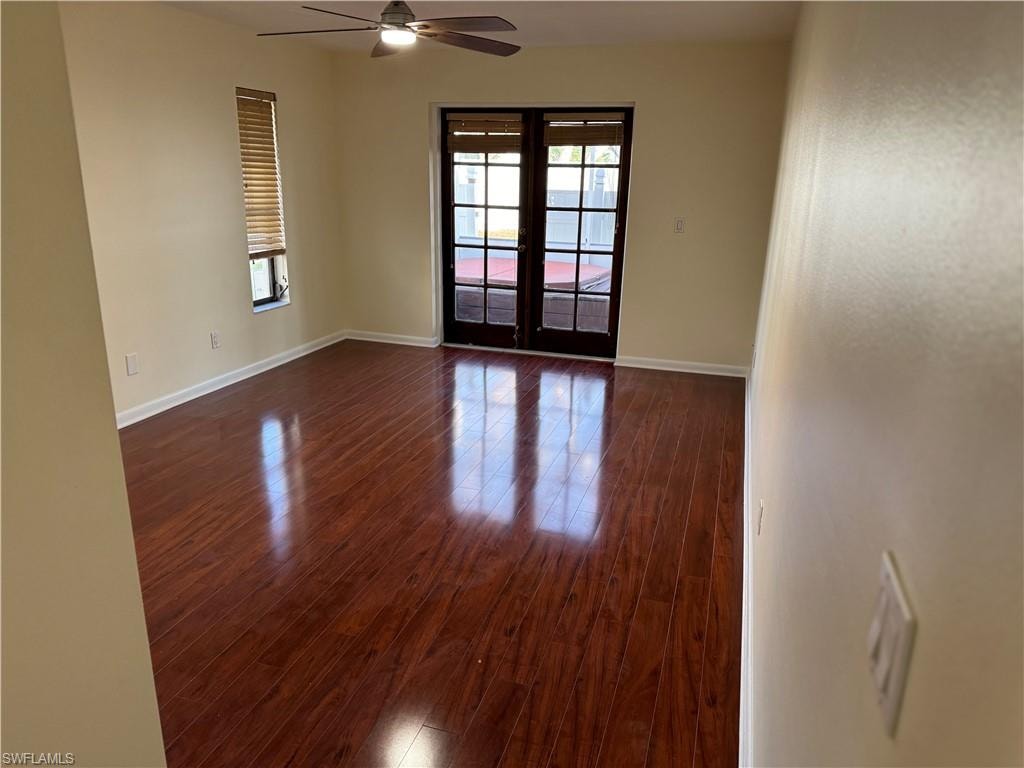 Spacious living area showcasing rich wood-finish flooring with a high-gloss polish, neutral wall finishes, and abundant natural light from dual glass-panel doors and transom window
