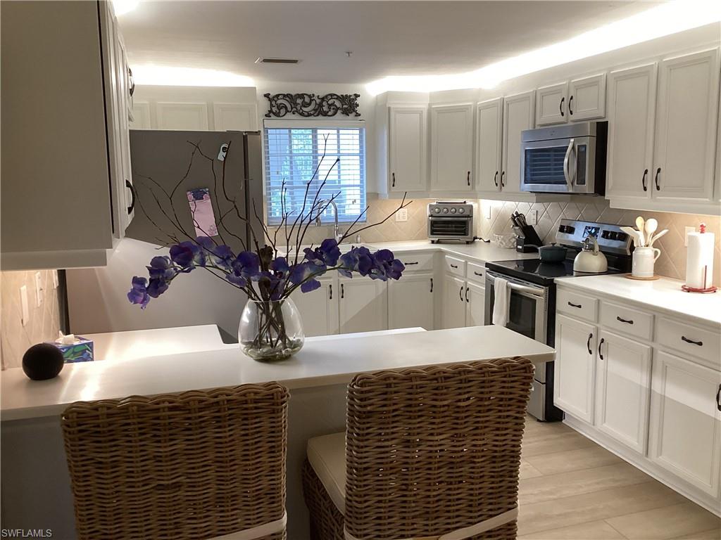Kitchen with appliances with stainless steel finishes, a peninsula, white cabinetry, backsplash, and a breakfast bar