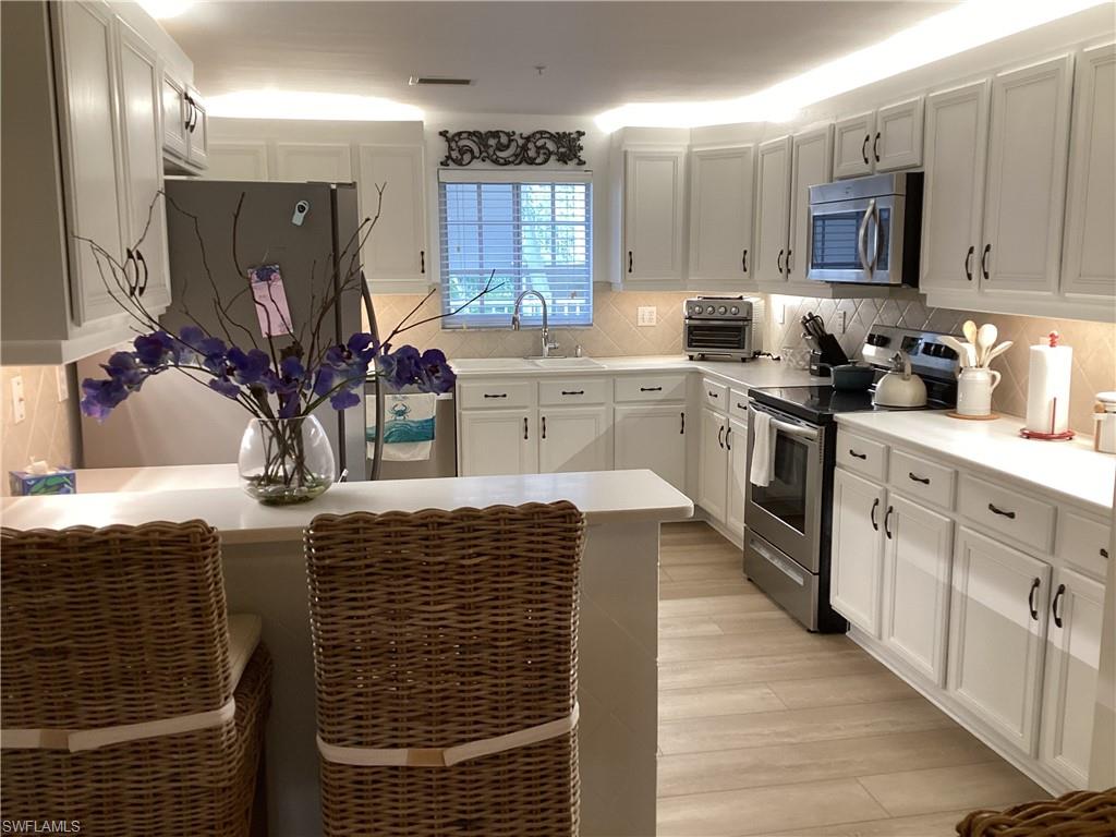 Kitchen with a peninsula, appliances with stainless steel finishes, light countertops, a breakfast bar area, and white cabinetry