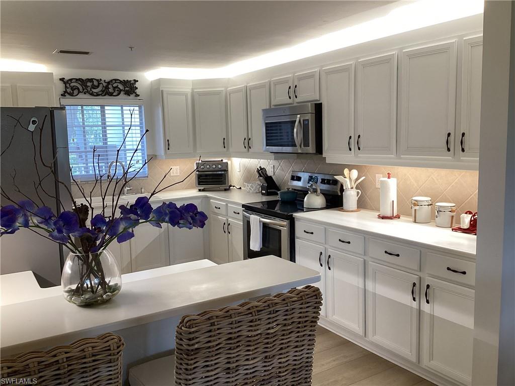 Kitchen with stainless steel appliances, light countertops, white cabinets, and backsplash