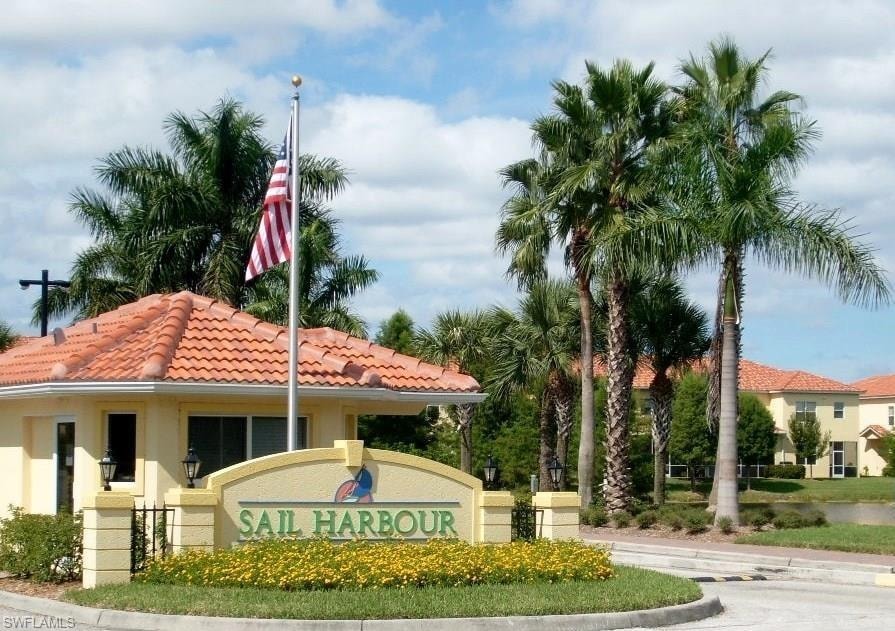 Entry monument with "SAIL HARBOUR" signage, framed by established palm trees and low-lying yellow flowering plants