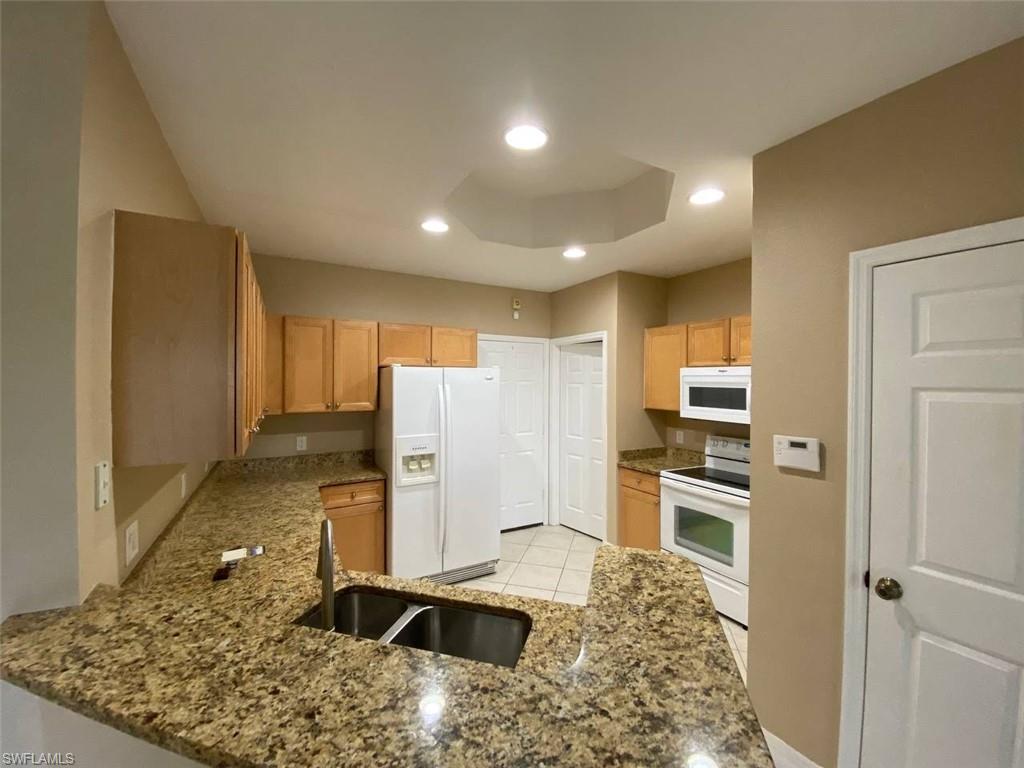 Kitchen featuring granite countertops, wood cabinetry, a dual basin stainless steel sink, and white appliances