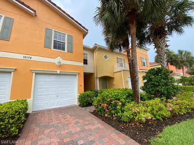 Paver driveway leading to a white garage door, set against an orange stucco exterior with decorative shutters