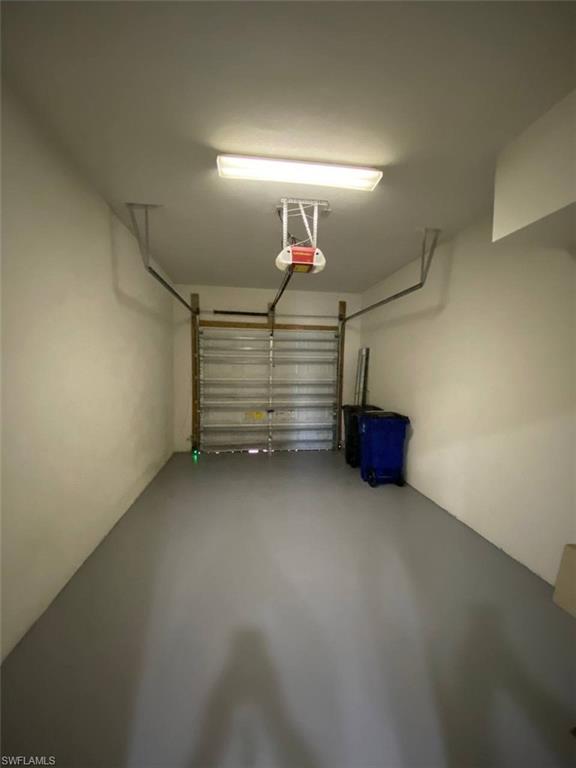 Attached garage with a roll-up door, neutral wall paint, and overhead fluorescent lighting