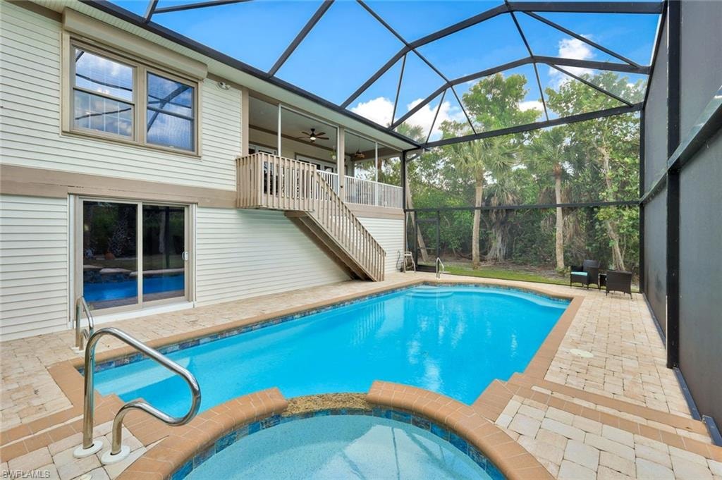 Screened lanai pool area featuring a resort-style swimming pool with curved edges, adjacent spa, paver decking, and an arched glass-panel enclosure