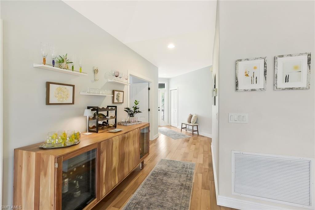 Modern kitchen and hallway featuring warm wood-finish cabinetry with integrated appliances, stainless steel hardware, and a sleek countertop