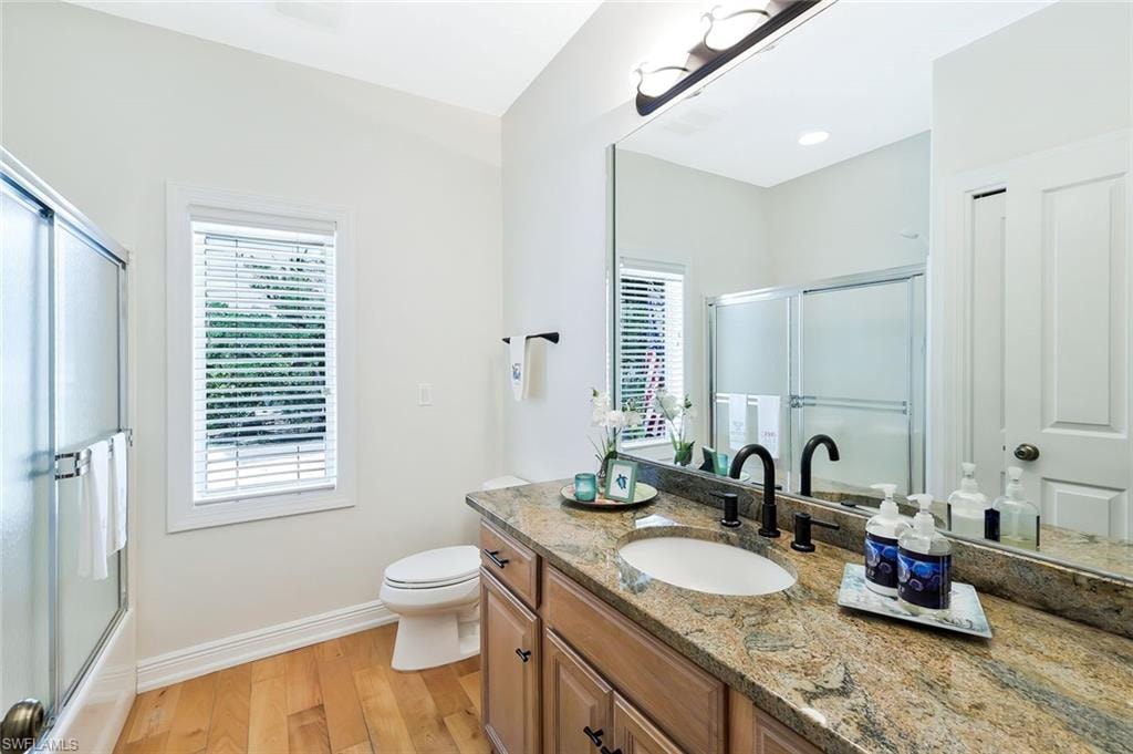 Spa-inspired primary bathroom featuring a dual-sink vanity with warm wood cabinetry, granite countertops, and matte black hardware