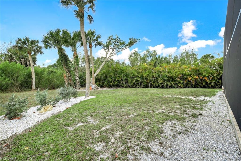 Expansive backyard showcasing mature palm and native trees, manicured lawn, and decorative stone hardscaping