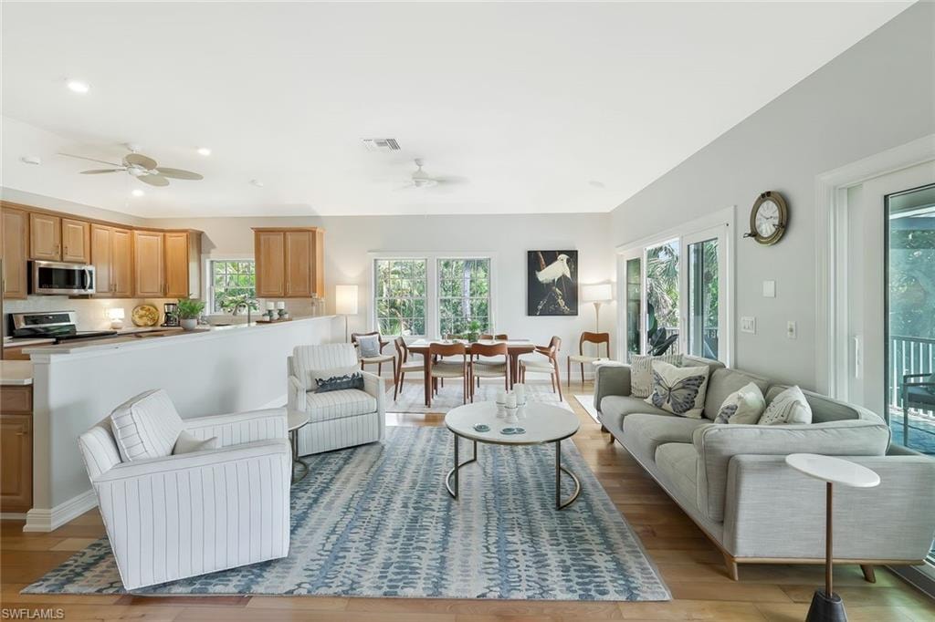Open-concept living space featuring hardwood flooring throughout, abundant natural light from multiple glass doors and windows, and a seamlessly integrated kitchen with wood cabinetry and stainless steel appliances