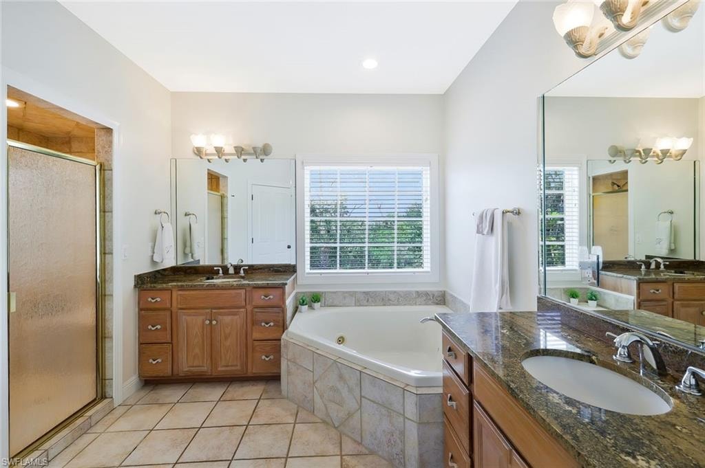 Spacious bathroom featuring a corner soaking tub, a separate glass-enclosed shower, dual vanity with granite countertops, and tile flooring
