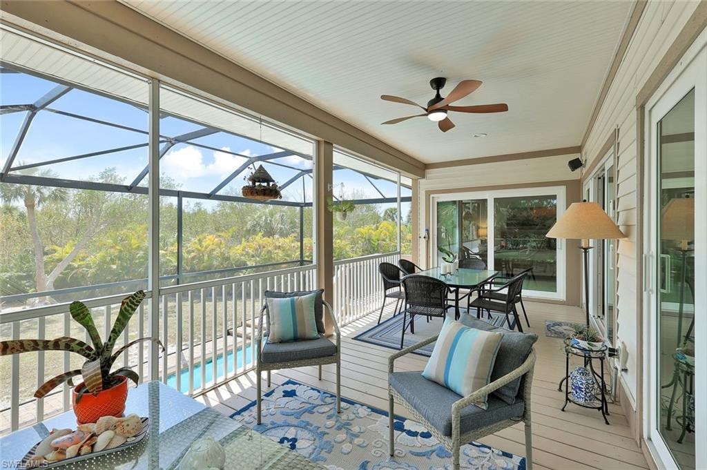 Screened sunroom with expansive windows framing natural woodland scenery, hardwood decking, ceiling fan with integrated lighting, and direct access to the home's interior through French doors