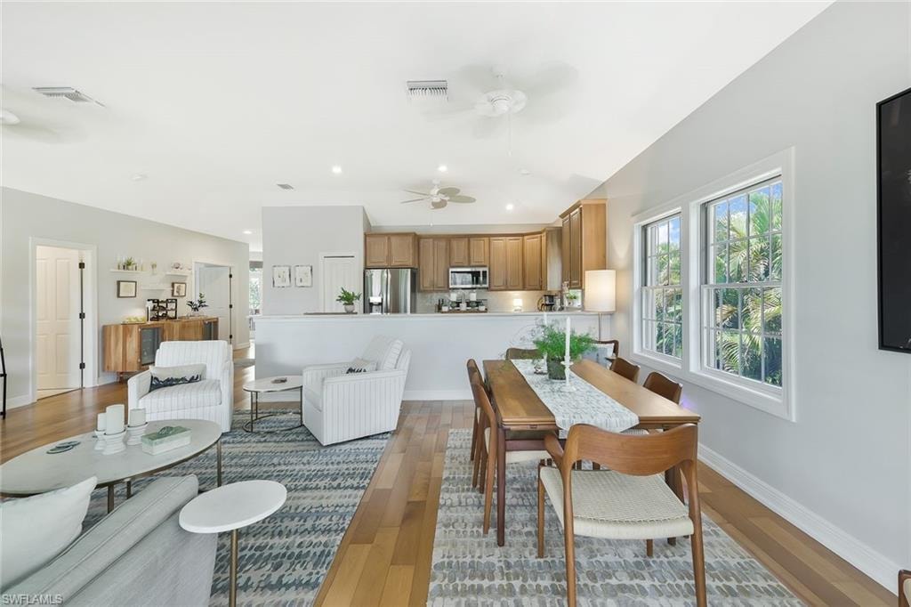 Open-concept living and dining area featuring wood-finish flooring, a neutral color palette, and abundant natural light from multi-panel glass doors and windows