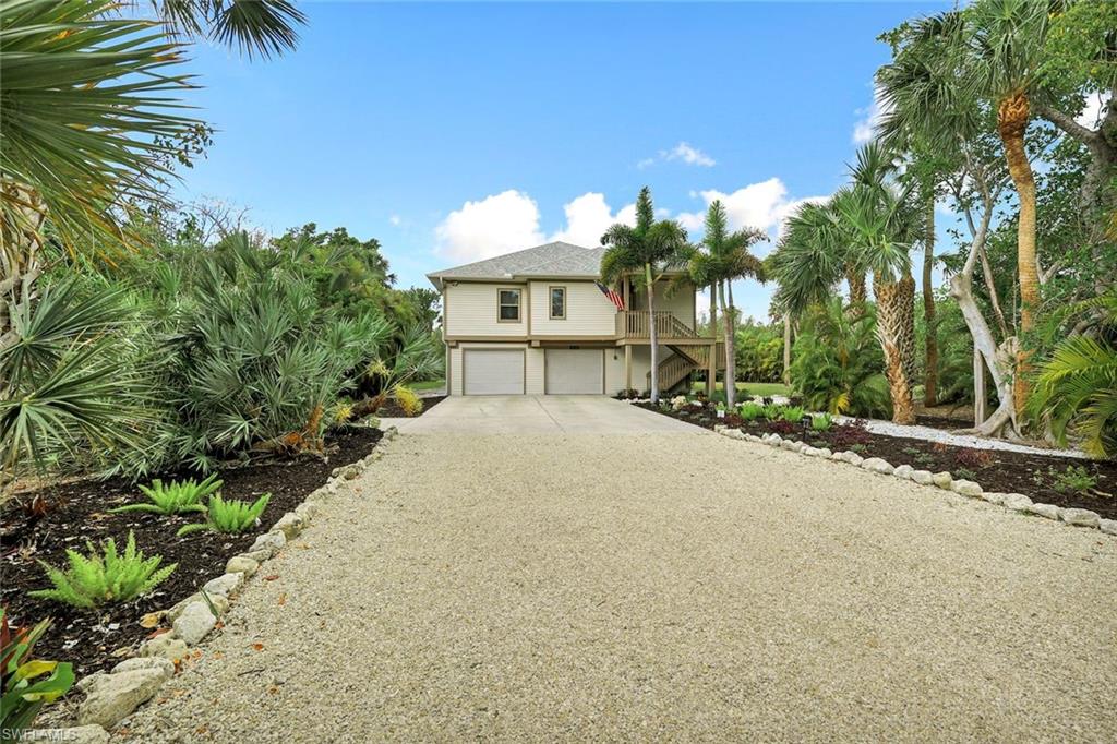 Striking two-story residence featuring a wide concrete driveway, two-car garage, and mature tropical landscaping including palm trees and native plantings