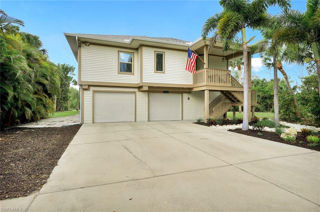 Elevated coastal home featuring a spacious two-car garage with concrete driveway, vinyl siding exterior, and a covered front porch with decorative railings