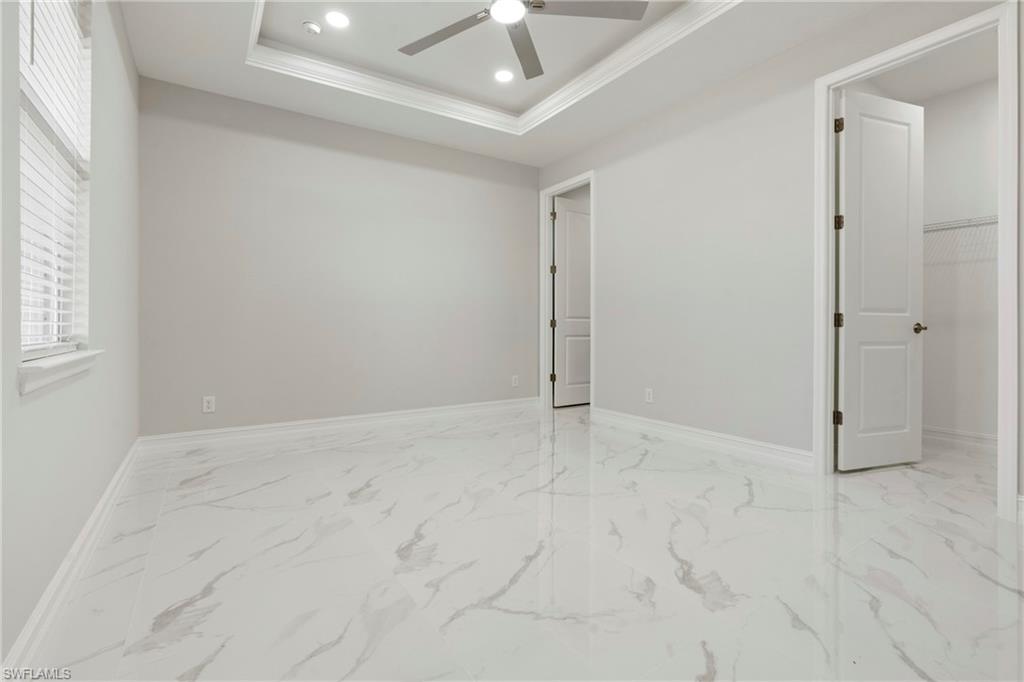 Spare room with a tray ceiling, marble finish floor, recessed lighting, ceiling fan, and baseboards
