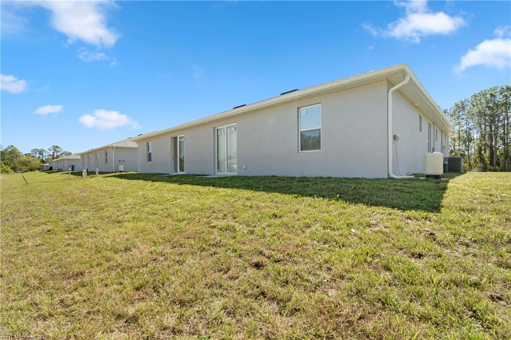 Back of property with central AC, a lawn, and stucco siding
