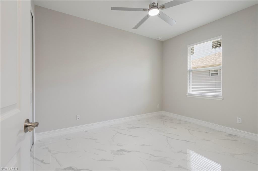 Empty room featuring a ceiling fan, marble finish floor, and baseboards