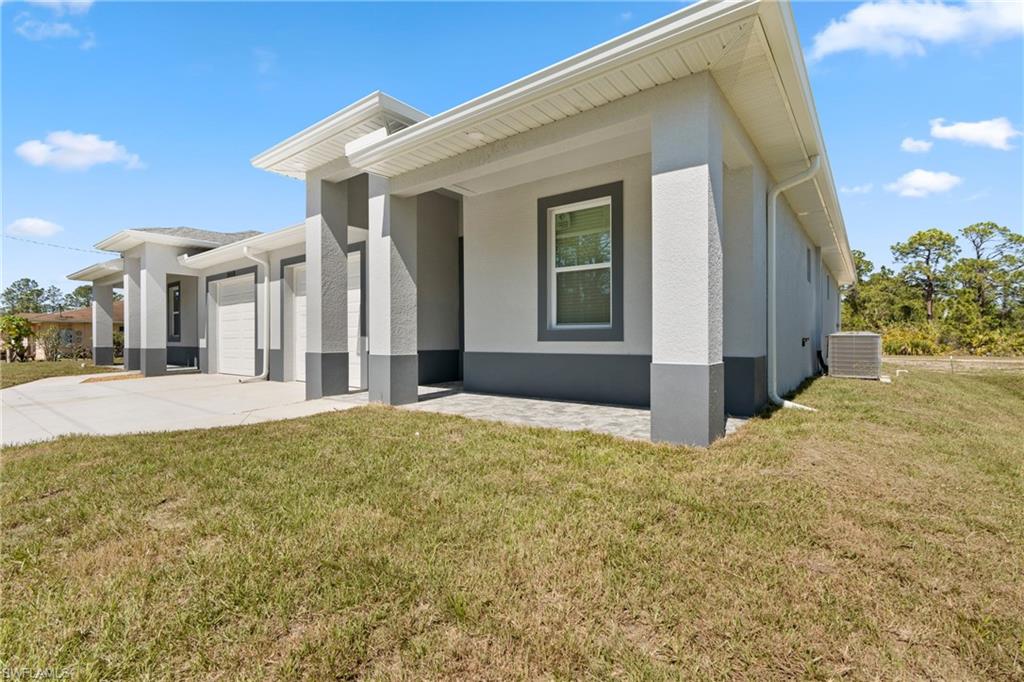 View of side of home featuring a garage, concrete driveway, cooling unit, a yard, and stucco siding