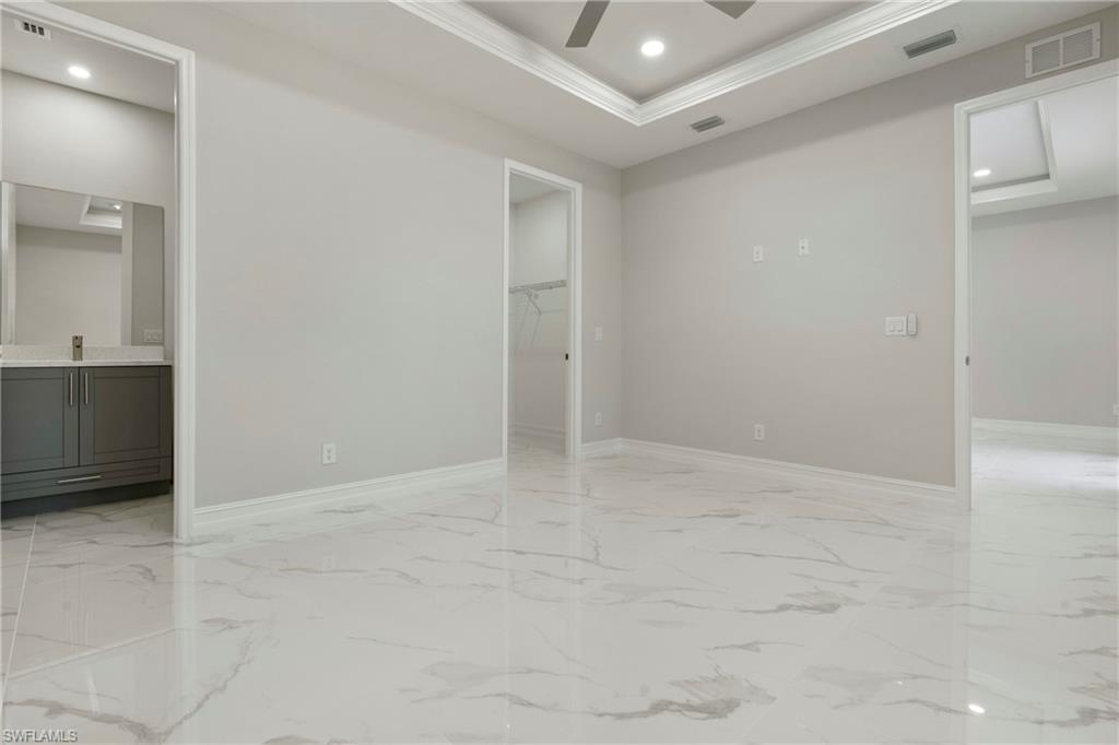 Empty room with a tray ceiling, marble finish floor, visible vents, and crown molding