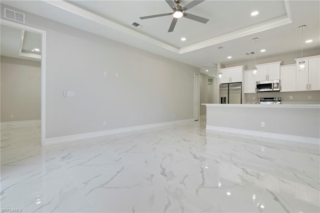 Unfurnished living room featuring visible vents, a tray ceiling, and baseboards