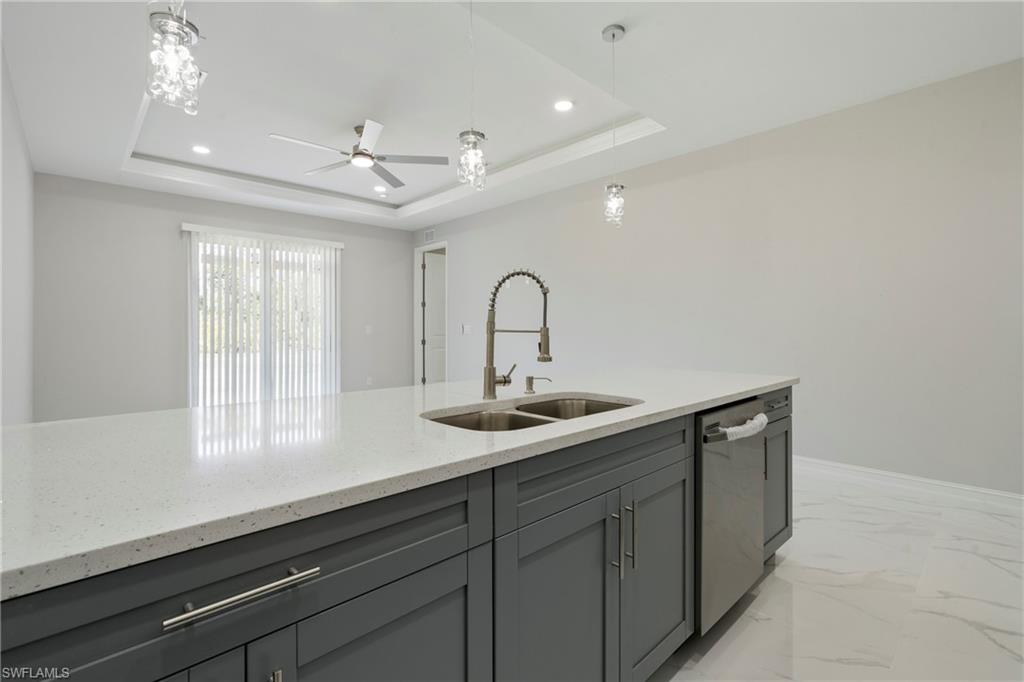Kitchen with a sink, marble finish floor, stainless steel dishwasher, gray cabinets, and a raised ceiling