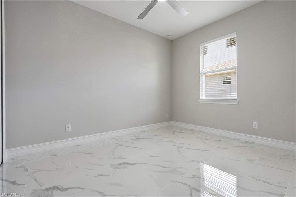 Unfurnished room with a ceiling fan, marble finish floor, and baseboards