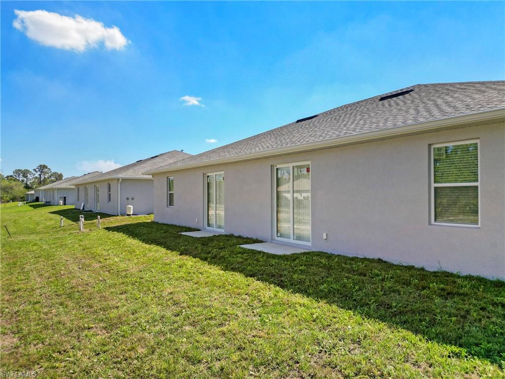 Back of house with a shingled roof, a lawn, and stucco siding