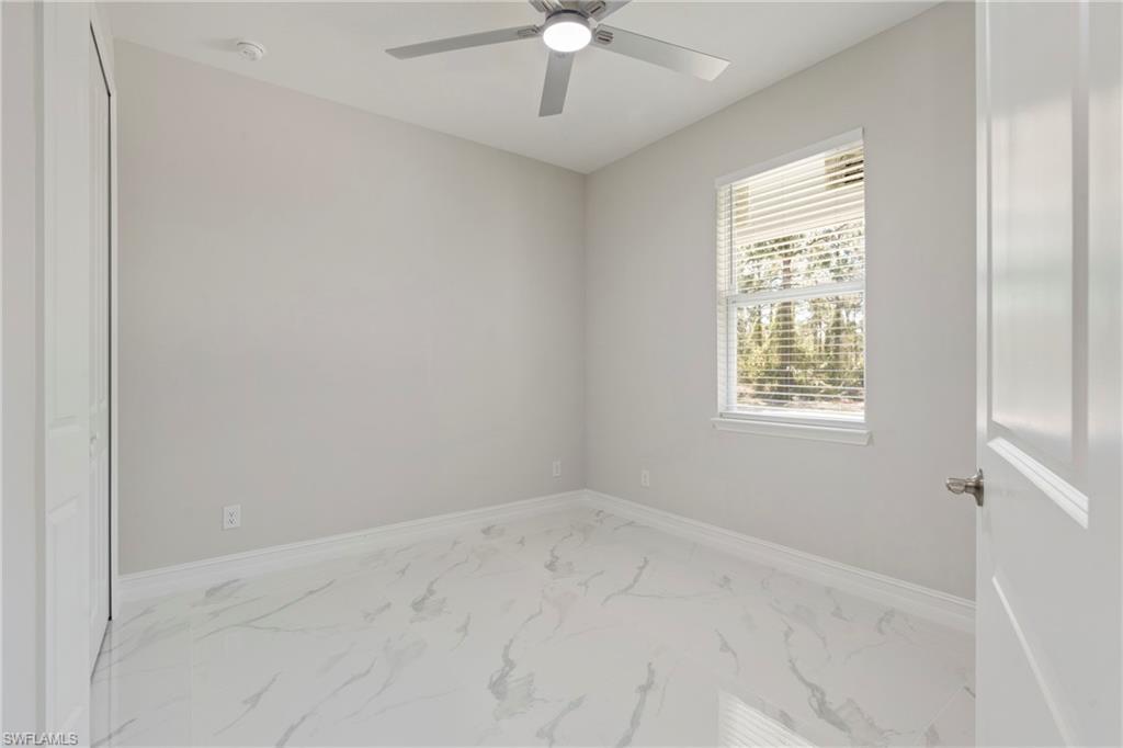 Spare room featuring marble finish floor, baseboards, and a ceiling fan