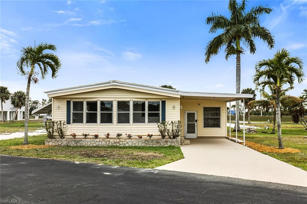 Single-story residence featuring light-colored siding, a covered carport, and multiple windows with dark shutters