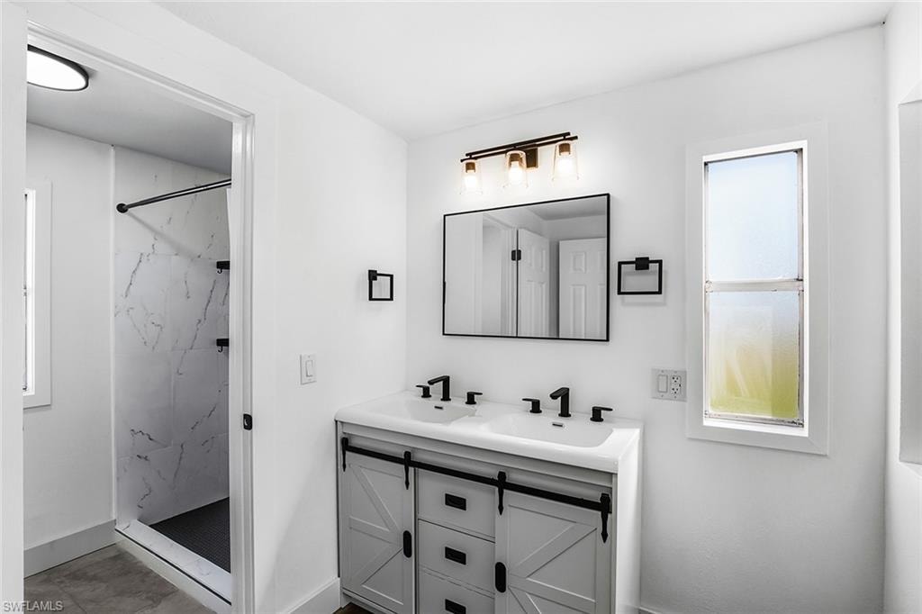 Bathroom featuring a dual-sink vanity with barn door style cabinetry, black hardware, and a framed mirror