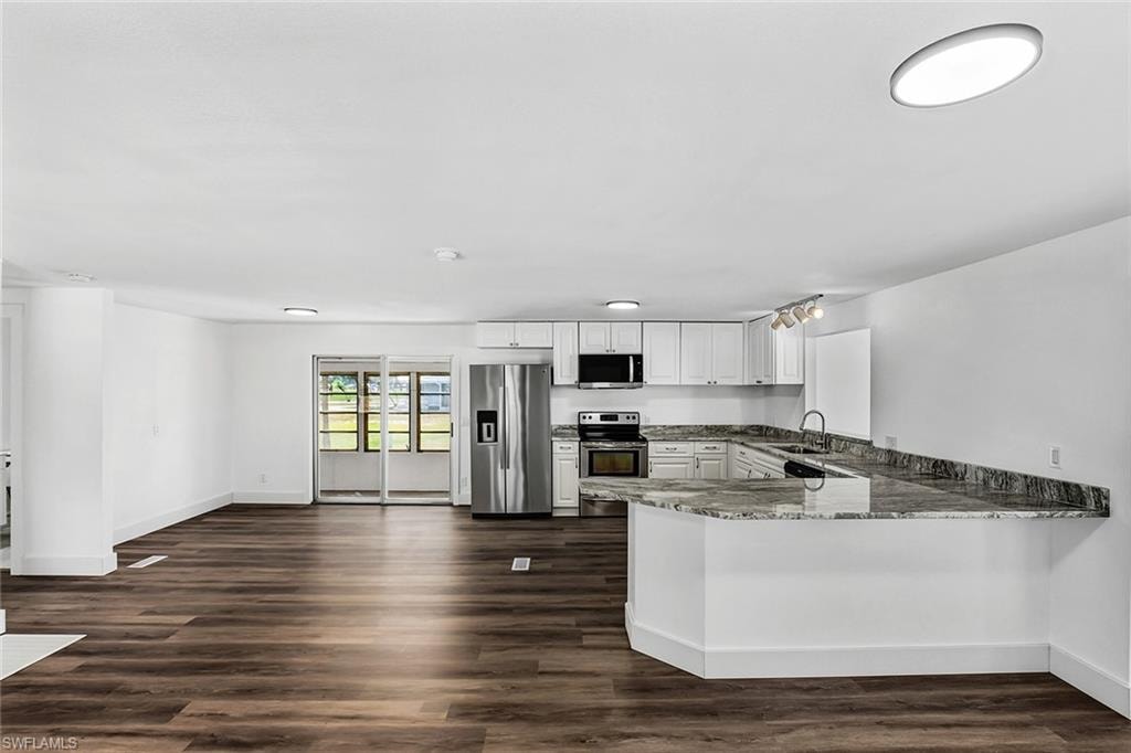 Expansive open-concept living area featuring wood-finish flooring, a contemporary kitchen with white cabinetry, stainless steel appliances, and a generously sized island with a stone countertop