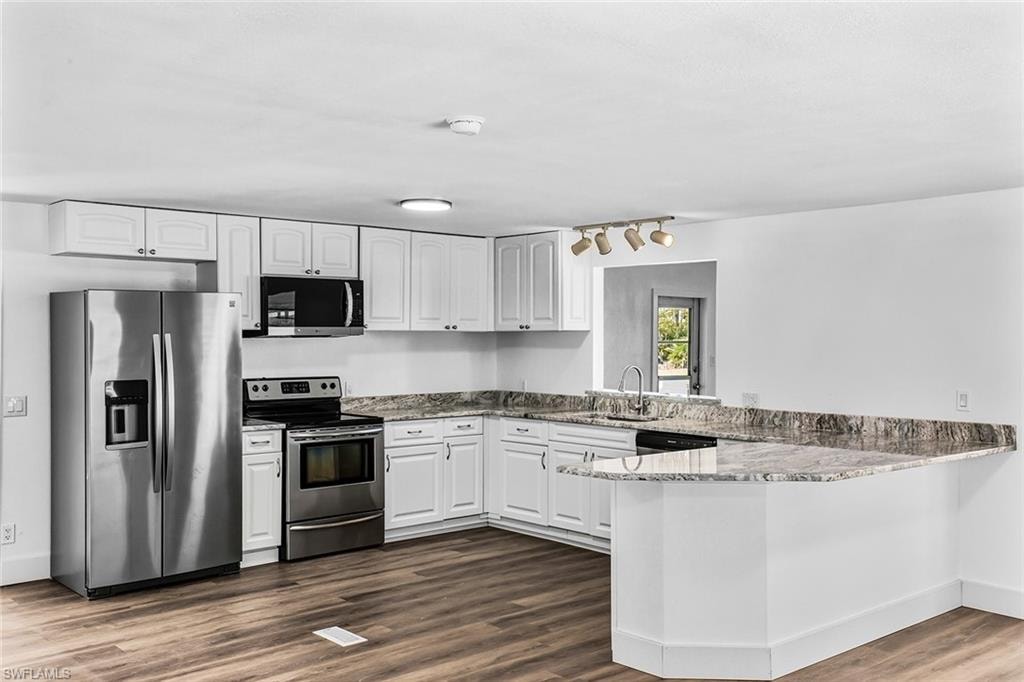 Kitchen featuring white cabinetry, stainless steel appliances, a corner sink with a gooseneck faucet, and wood-finish flooring