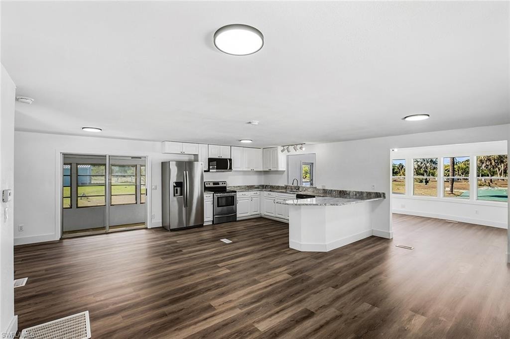Open-concept living space with wood-finish flooring, white cabinetry, stainless steel appliances, and a granite-look countertop island