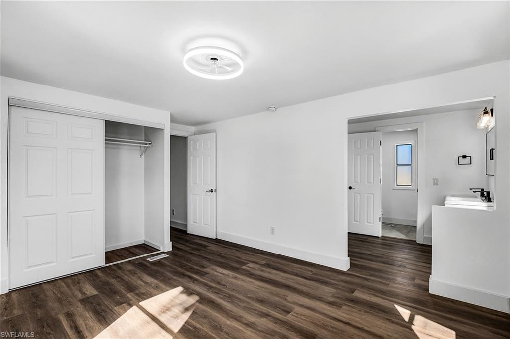 Spacious room featuring wood-finish flooring, bright white walls, and a contemporary ceiling light fixture